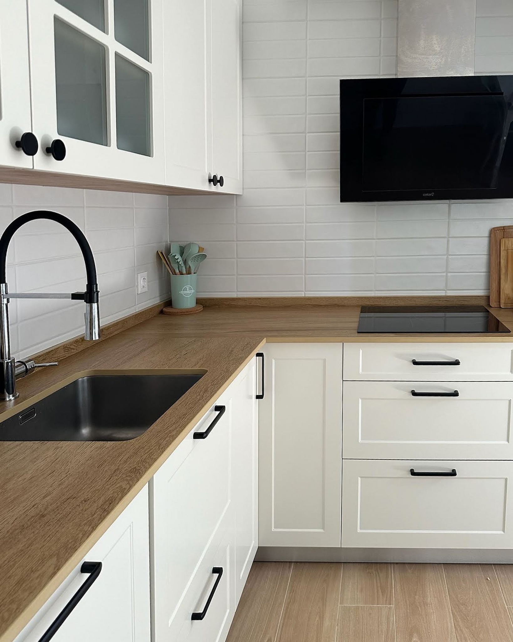 Cocina blanca con encimera de madera y grifo negro moderno.