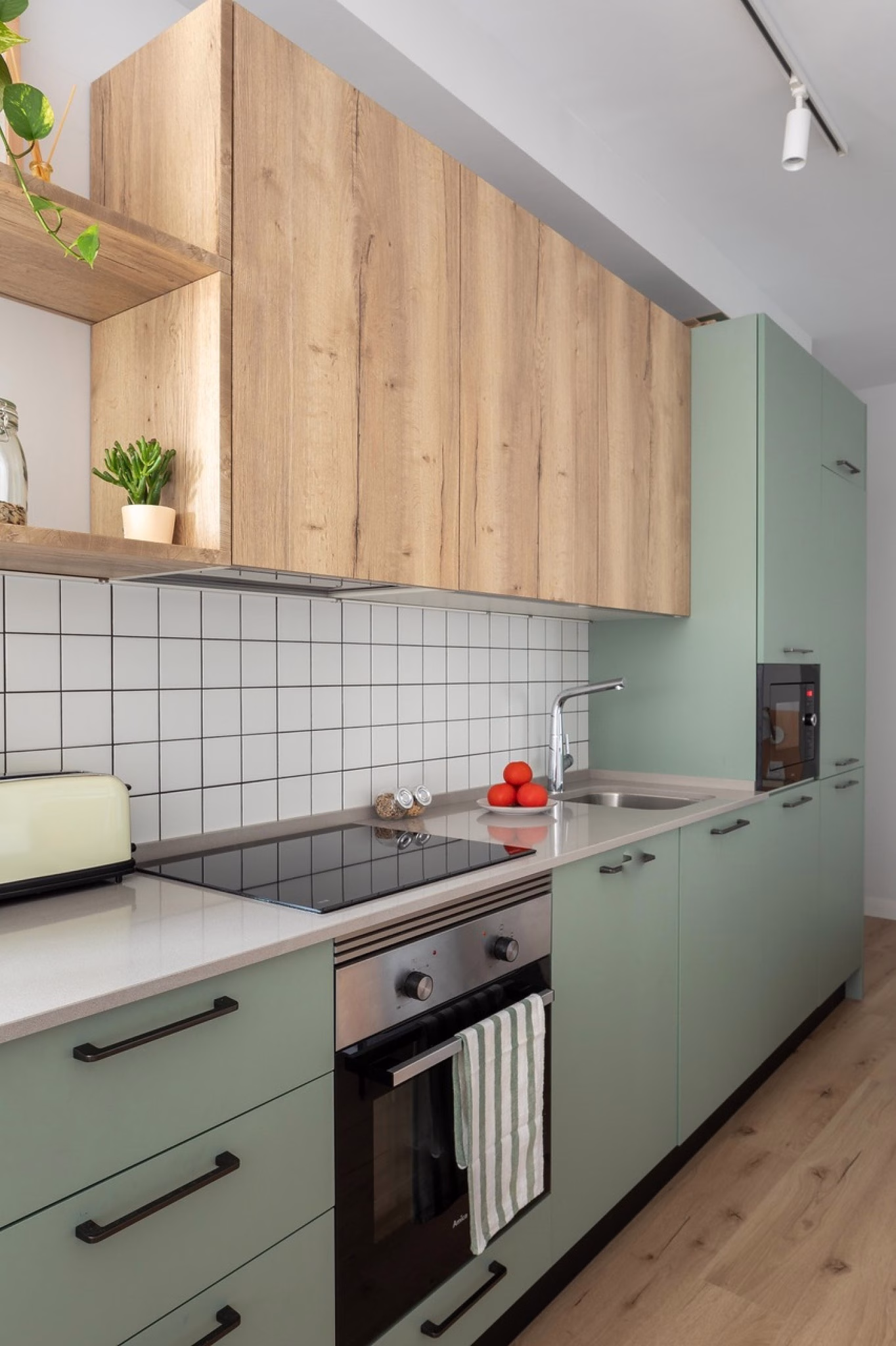 Cocina moderna verde con muebles de madera y encimera clara.