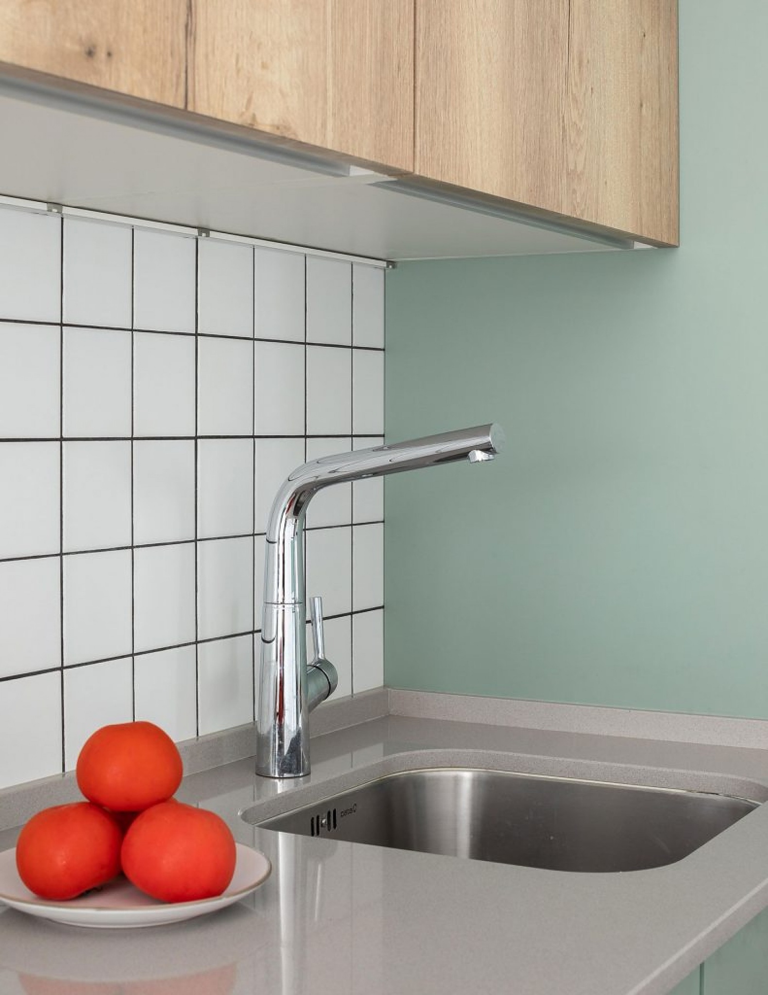 Detalle de fregadero de cocina con encimera clara, azulejos blancos y pared verde menta.