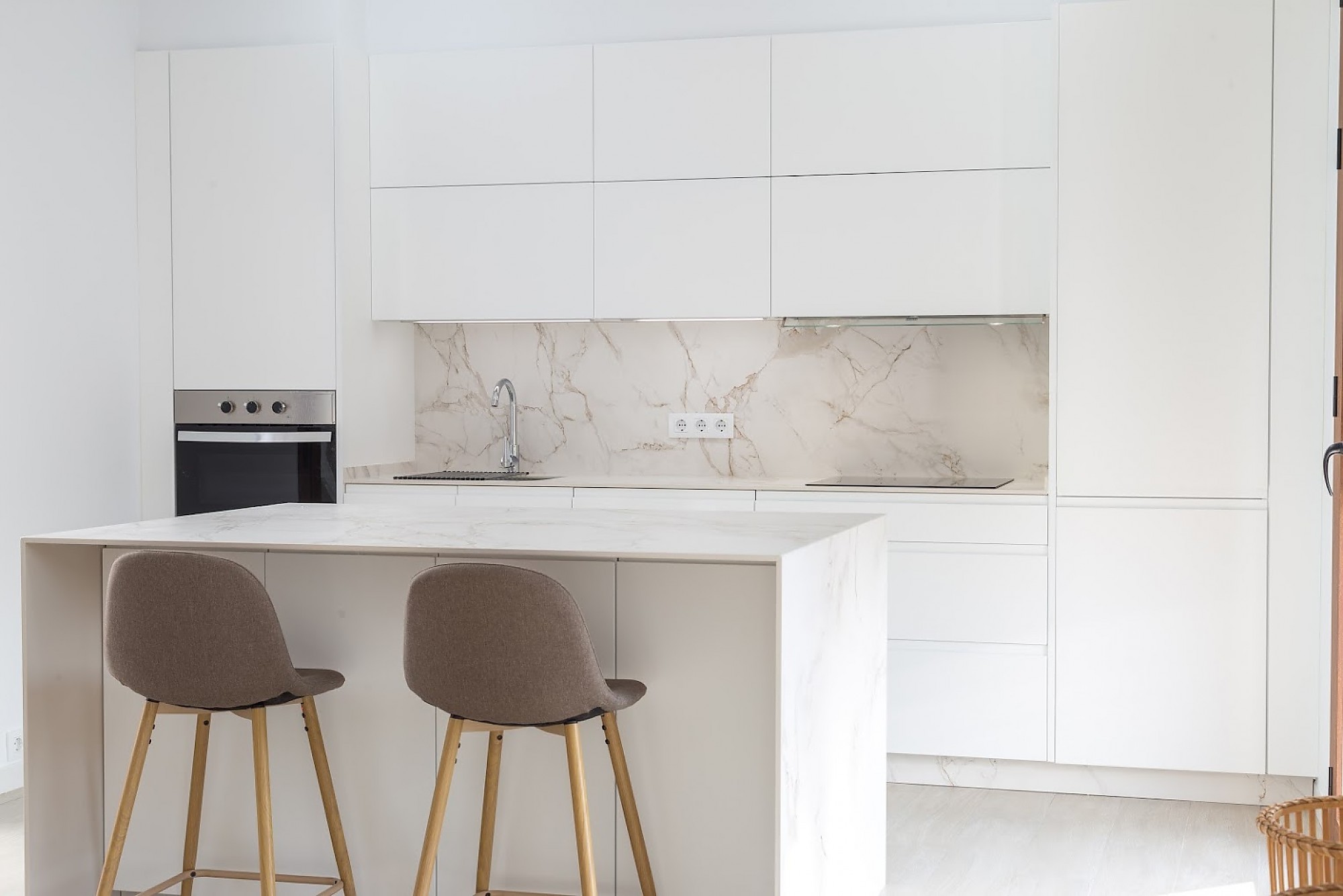 Cocina blanca minimalista con isla de mármol y barra para desayunos.