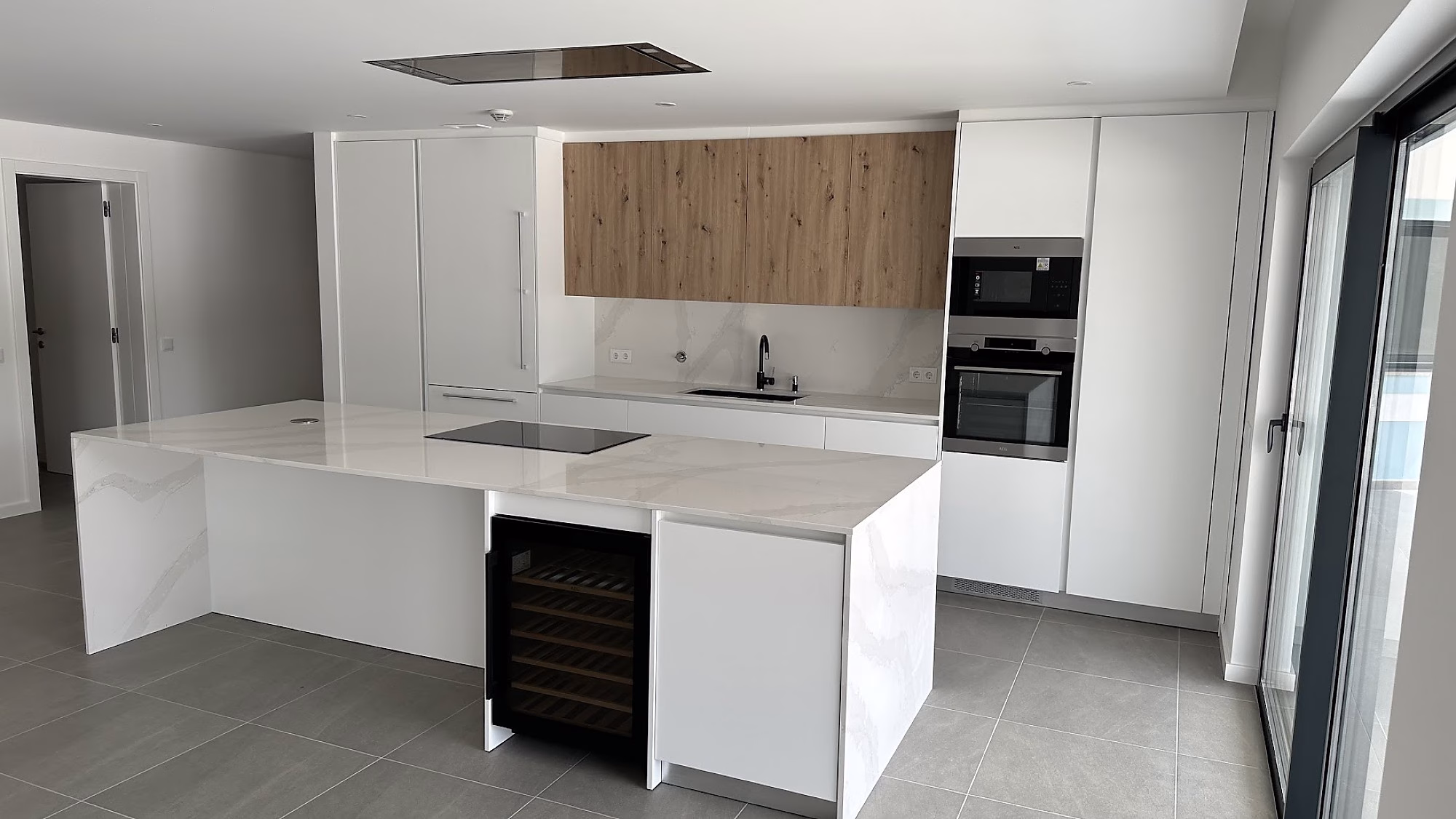 Cocina moderna blanca con isla de mármol y muebles altos en madera.