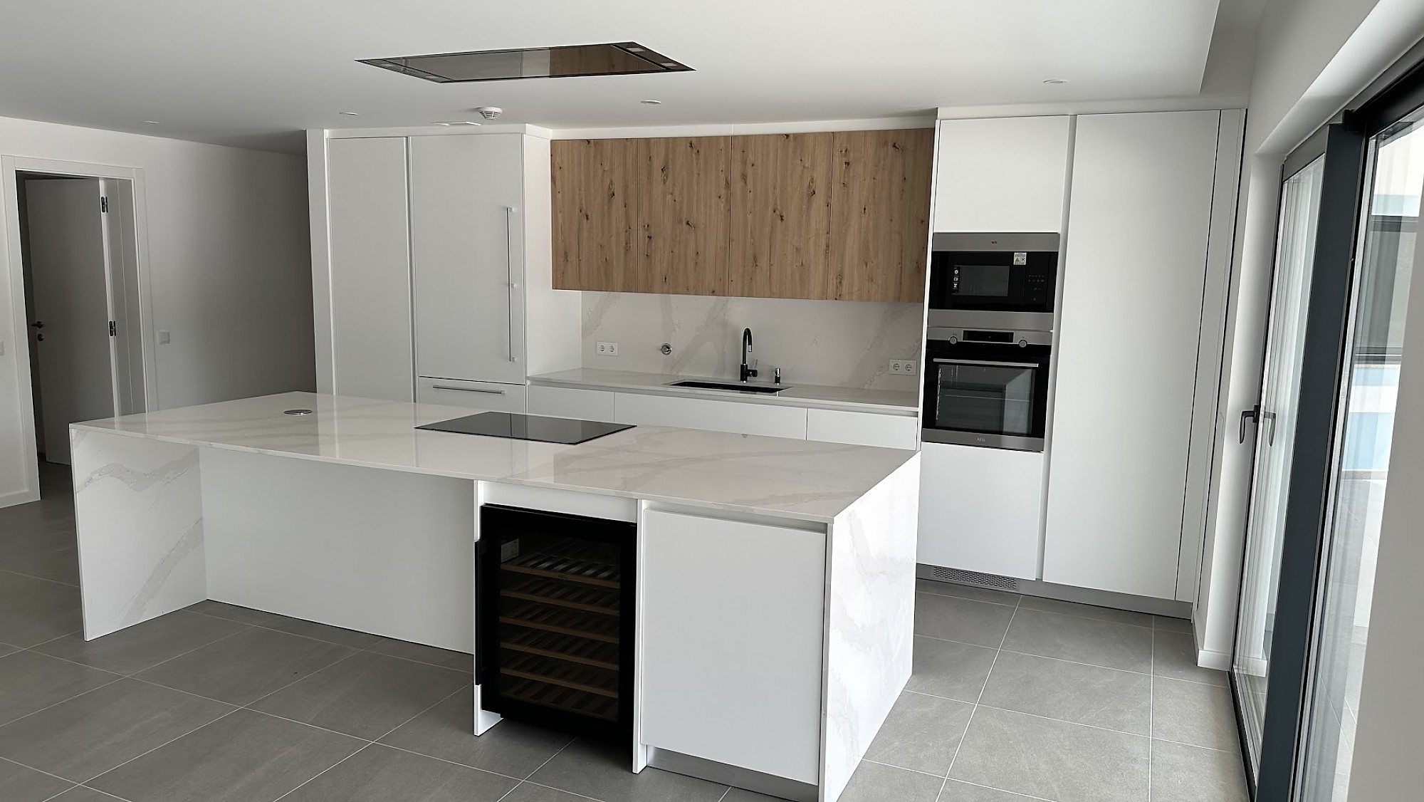 Cocina moderna blanca con isla de mármol y muebles altos en madera.