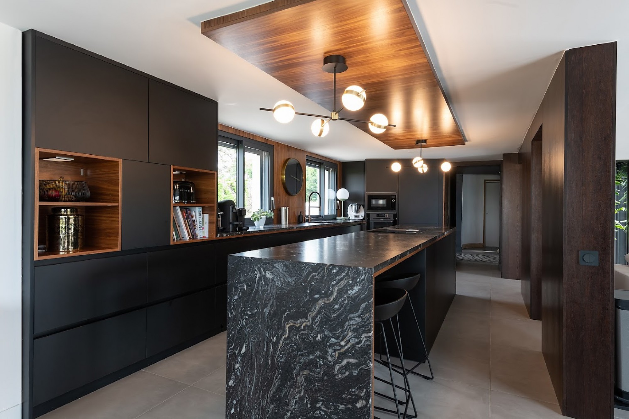 Cocina moderna en negro y madera con isla de mármol oscuro y luminarias de diseño