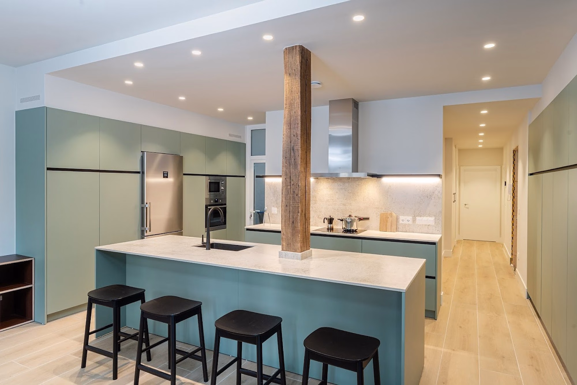 Cocina moderna verde con isla central y columna de madera.