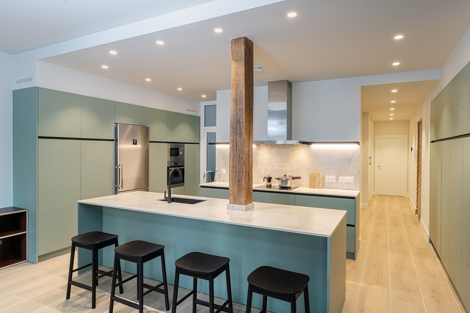 Cocina moderna verde con isla central y columna de madera.
