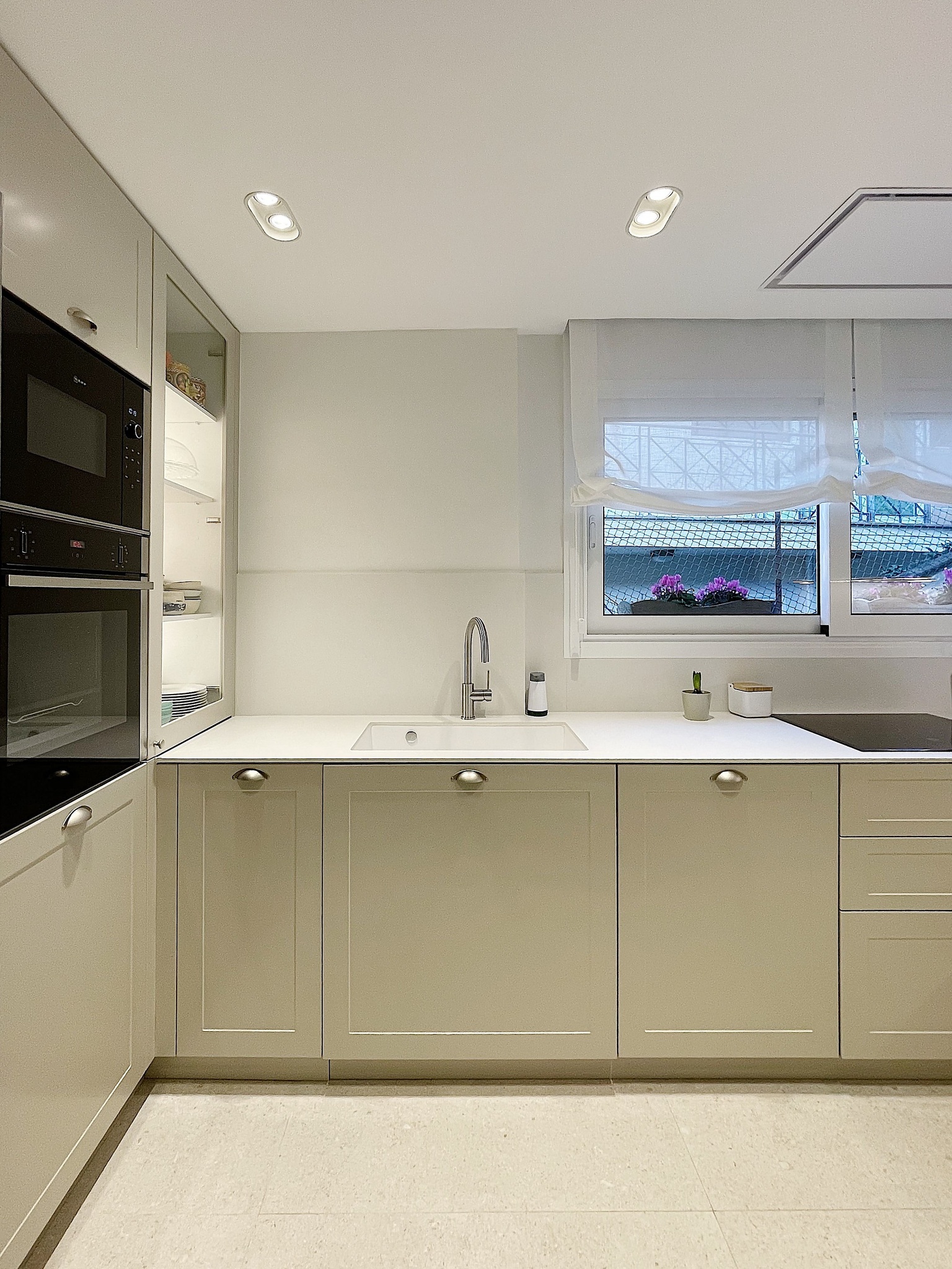 Cocina moderna beige con encimera blanca y horno empotrado.